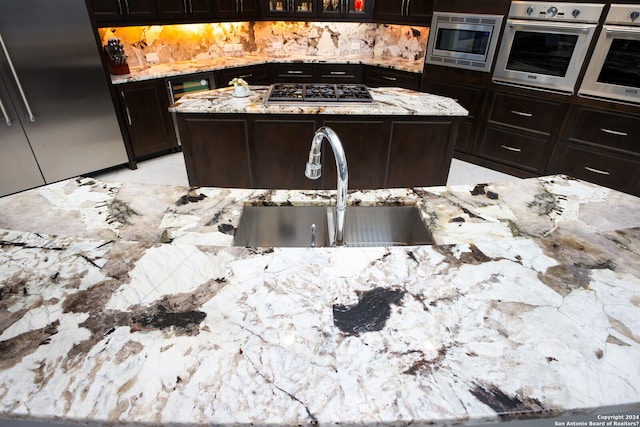 kitchen with stainless steel appliances, light tile floors, a center island, light stone counters, and sink