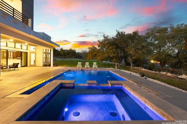 pool at dusk with an in ground hot tub, pool water feature, and a patio