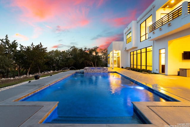 pool at dusk featuring pool water feature and a patio