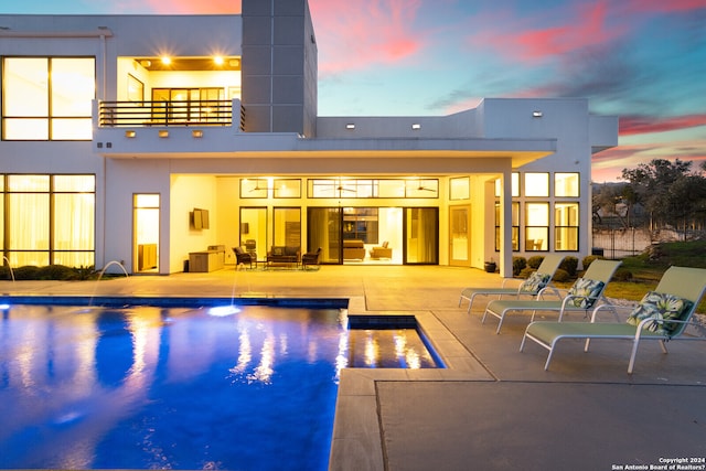 pool at dusk with pool water feature and a patio area