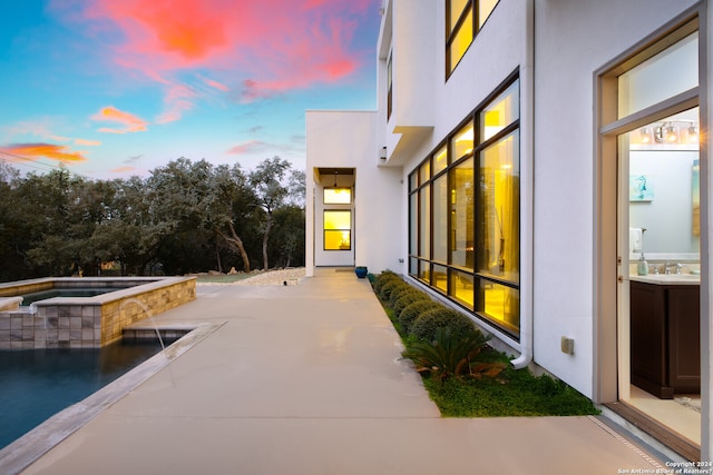 exterior space featuring a patio area, an in ground hot tub, pool water feature, and sink