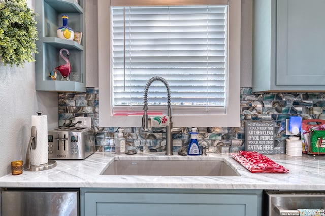 kitchen featuring light stone countertops, backsplash, gray cabinets, and sink