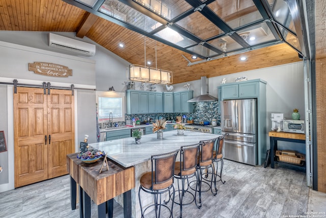 kitchen featuring beamed ceiling, a barn door, light stone countertops, stainless steel fridge, and wall chimney range hood