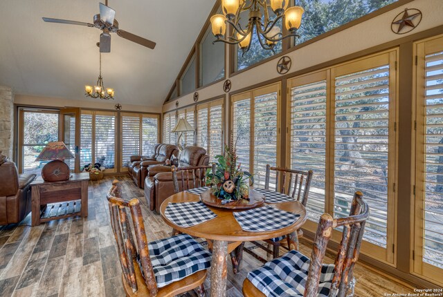 dining area featuring high vaulted ceiling, ceiling fan with notable chandelier, and wood-type flooring