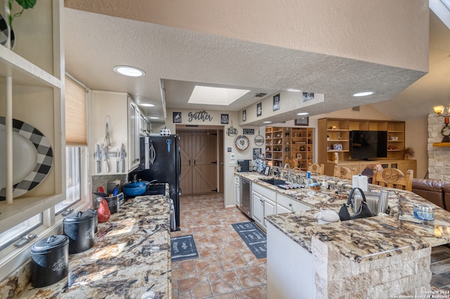 kitchen with a skylight, a textured ceiling, light stone countertops, and kitchen peninsula