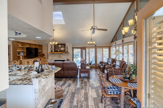 living room featuring high vaulted ceiling, ceiling fan with notable chandelier, a stone fireplace, built in features, and dark hardwood / wood-style floors