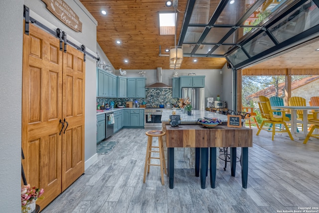 kitchen featuring a barn door, a kitchen bar, stainless steel appliances, wall chimney exhaust hood, and backsplash