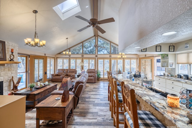 dining room with a skylight, a stone fireplace, plenty of natural light, and ceiling fan with notable chandelier