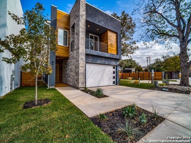contemporary house with a balcony, a front yard, and a garage