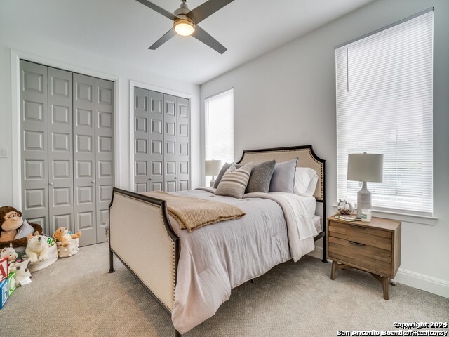 carpeted bedroom with ceiling fan and multiple closets