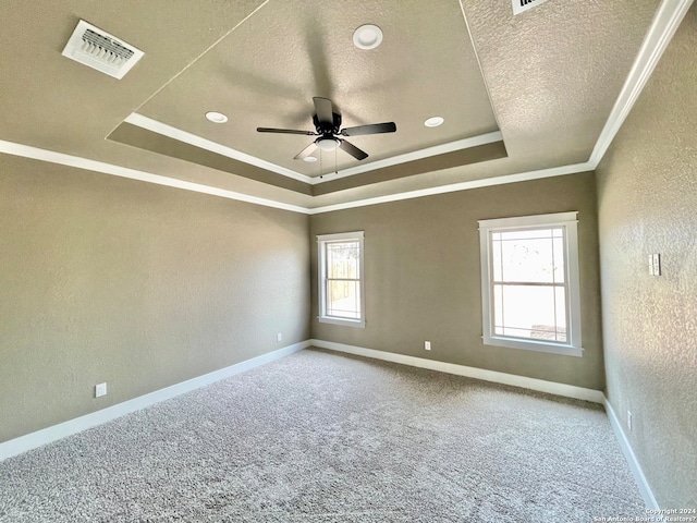 carpeted empty room with ceiling fan, crown molding, a wealth of natural light, and a raised ceiling