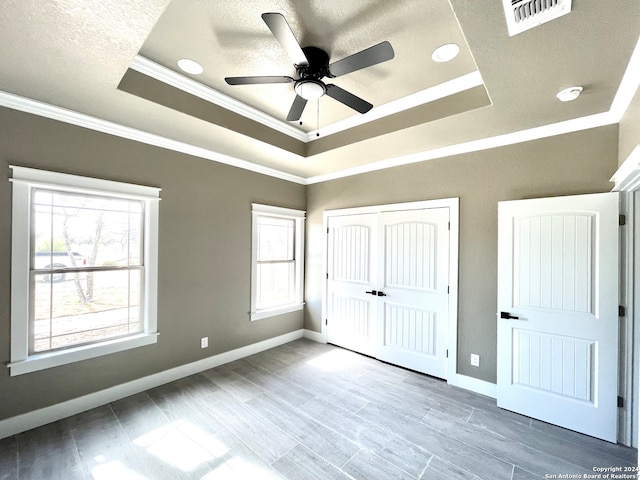 unfurnished bedroom featuring light hardwood / wood-style floors, a closet, ceiling fan, ornamental molding, and a raised ceiling