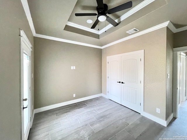 unfurnished bedroom with ceiling fan, ornamental molding, a tray ceiling, and a closet