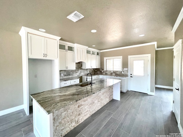 kitchen with white cabinets, an island with sink, and ornamental molding