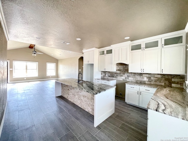 kitchen featuring white cabinets, ceiling fan, light stone countertops, and vaulted ceiling