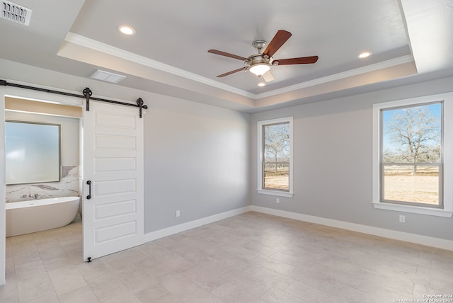 unfurnished bedroom featuring a barn door, a tray ceiling, and ensuite bathroom