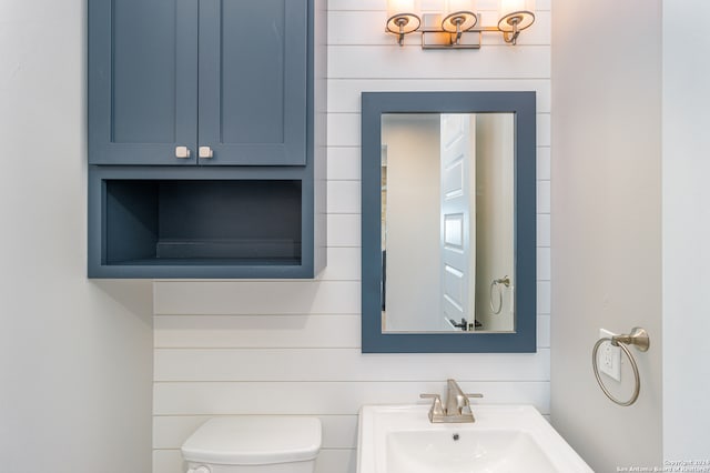 bathroom with toilet, wood walls, and sink