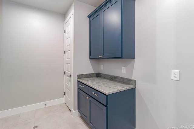 kitchen featuring light tile patterned floors, blue cabinets, and light stone counters