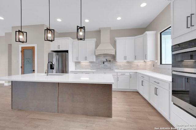 kitchen with white cabinetry, backsplash, premium range hood, stainless steel appliances, and light hardwood / wood-style floors