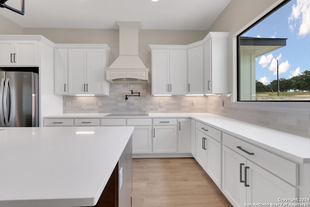 kitchen with decorative backsplash, stainless steel fridge, custom range hood, and plenty of natural light