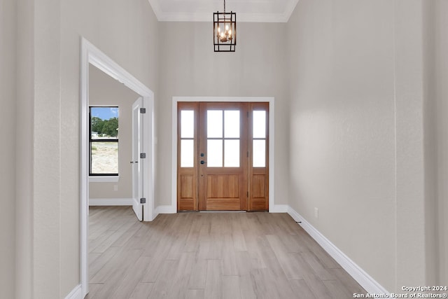 foyer entrance with an inviting chandelier, a high ceiling, ornamental molding, and light hardwood / wood-style floors