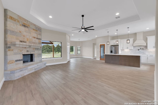 unfurnished living room featuring a stone fireplace, light hardwood / wood-style flooring, ceiling fan, and a raised ceiling