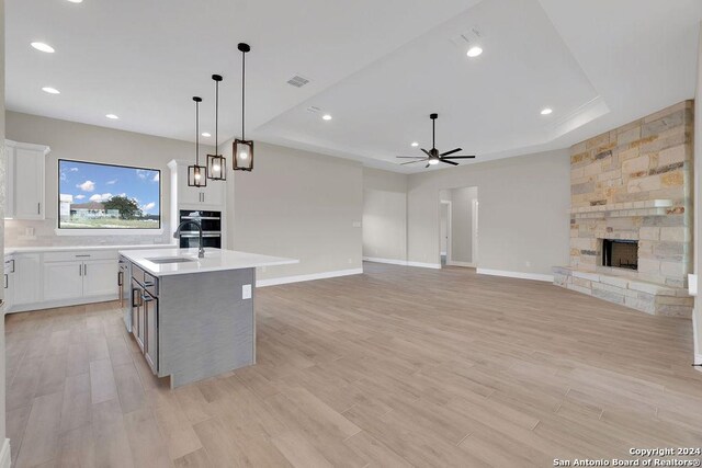 kitchen featuring white cabinetry, ceiling fan, light hardwood / wood-style floors, a fireplace, and a center island with sink