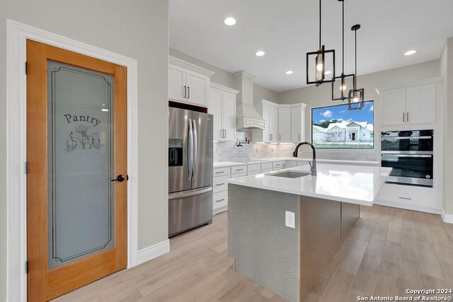 kitchen with custom range hood, light hardwood / wood-style flooring, an island with sink, appliances with stainless steel finishes, and sink