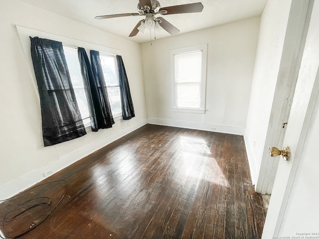 empty room featuring ceiling fan, dark wood-type flooring, and a wealth of natural light