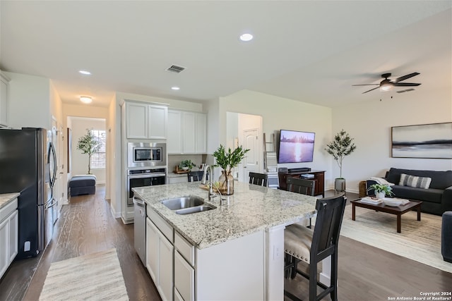 kitchen featuring white cabinetry, ceiling fan, stainless steel appliances, a center island with sink, and light stone counters