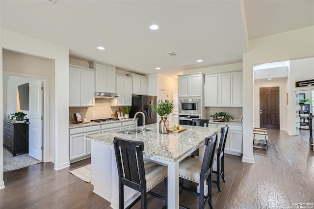 kitchen featuring an island with sink, sink, appliances with stainless steel finishes, dark wood-type flooring, and tasteful backsplash