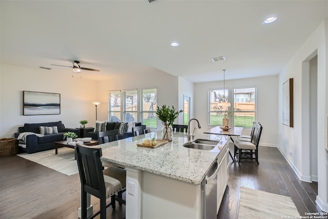 kitchen with light stone countertops, ceiling fan with notable chandelier, a center island with sink, white cabinets, and sink