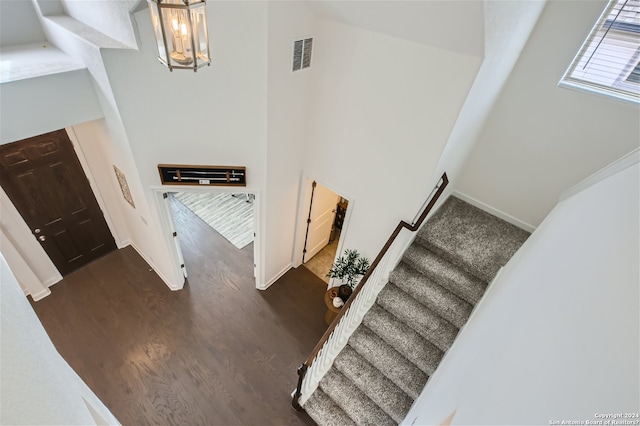 staircase featuring an inviting chandelier, dark wood-type flooring, and a towering ceiling