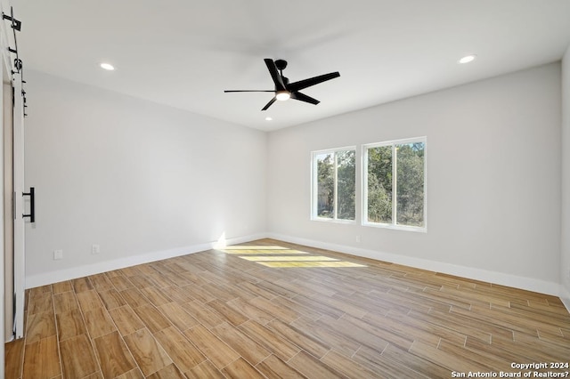 empty room featuring a barn door, ceiling fan, and light wood-type flooring