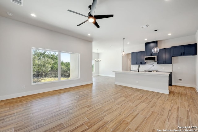 kitchen with ceiling fan with notable chandelier, a center island with sink, backsplash, hanging light fixtures, and sink