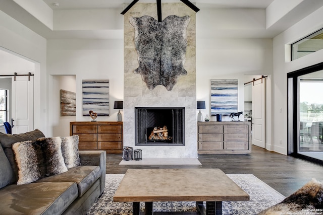 living room featuring a barn door, a premium fireplace, dark wood-type flooring, and a raised ceiling