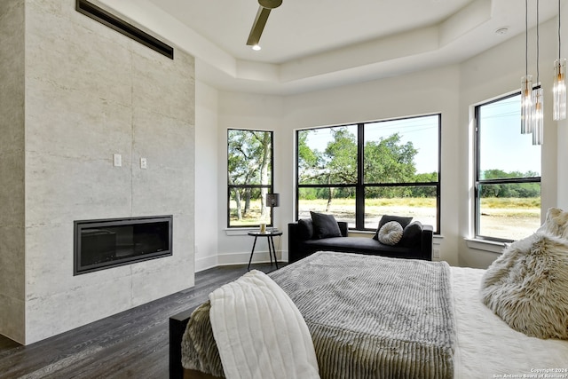 bedroom featuring a tile fireplace, a raised ceiling, ceiling fan, and dark hardwood / wood-style floors