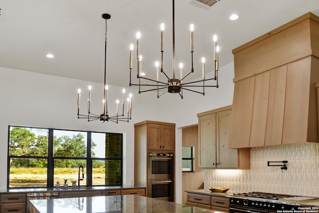 kitchen featuring tasteful backsplash, sink, stainless steel double oven, dark stone countertops, and an inviting chandelier