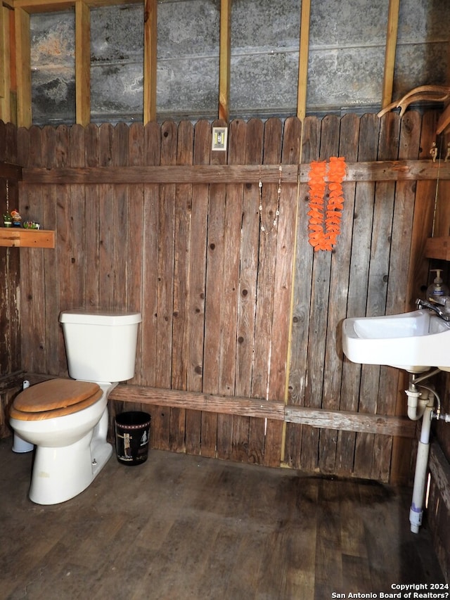 bathroom featuring toilet, wood walls, hardwood / wood-style floors, and sink