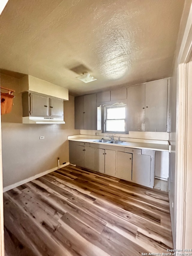 kitchen with gray cabinetry, a textured ceiling, wood-type flooring, and sink