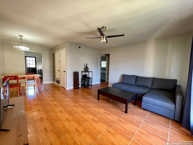 living room with light wood-type flooring, ceiling fan, and a textured ceiling