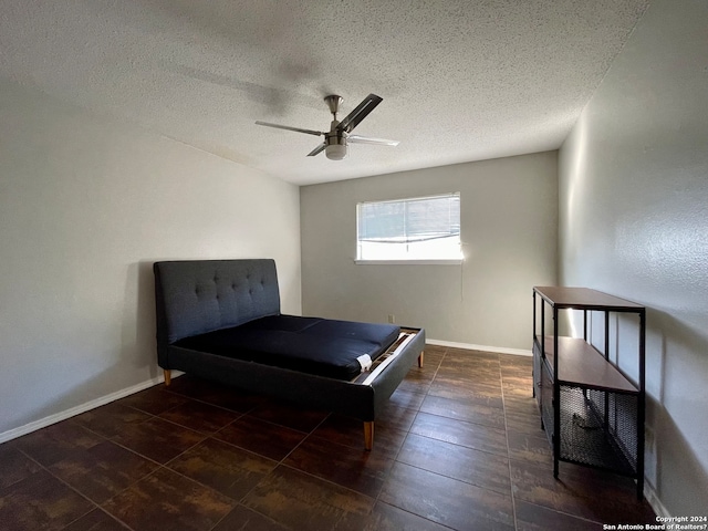 unfurnished bedroom featuring ceiling fan, a textured ceiling, and dark tile flooring