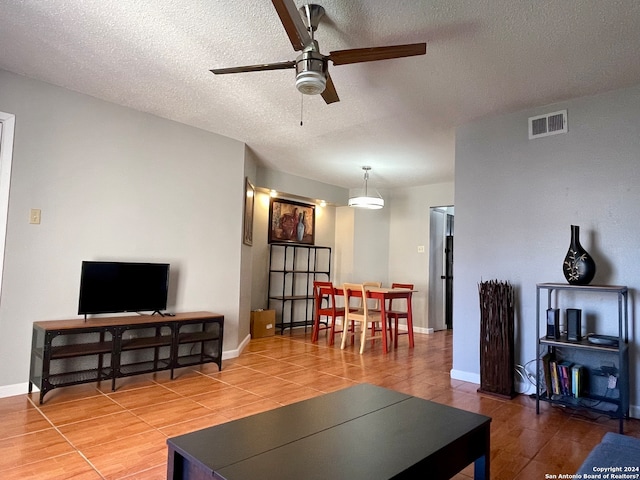 living room featuring light tile floors, ceiling fan, and a textured ceiling