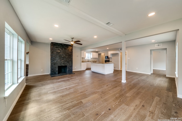 unfurnished living room with plenty of natural light, dark hardwood / wood-style floors, ceiling fan, and a stone fireplace