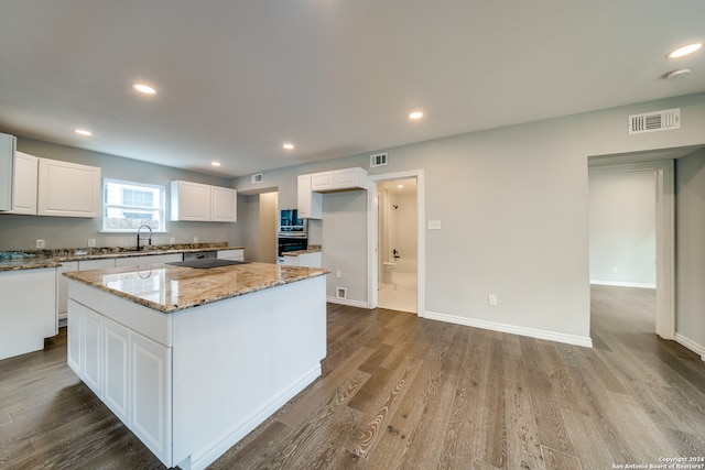 kitchen with white cabinetry, wood-type flooring, sink, light stone counters, and a kitchen island