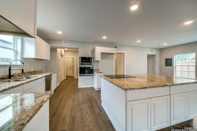 kitchen with light stone countertops, a kitchen island, white cabinetry, and sink