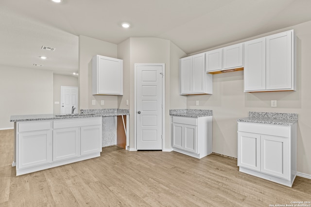 kitchen with light stone counters, light hardwood / wood-style floors, white cabinetry, and sink