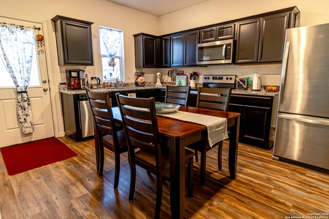 kitchen with dark brown cabinets, dark hardwood / wood-style flooring, stainless steel appliances, and light stone counters