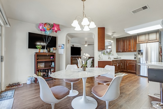 dining space featuring sink, light hardwood / wood-style flooring, and ceiling fan with notable chandelier