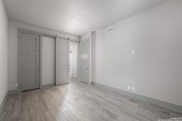 unfurnished bedroom with a barn door, light hardwood / wood-style floors, and a textured ceiling